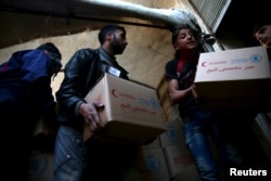 Men unload aid boxes from a Red Crescent aid convoy in the rebel held besieged town of Jesreen, in the eastern Damascus suburb of Ghouta, Syria, March 7, 2016.