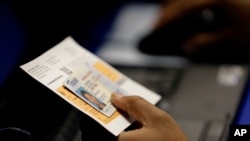File - An election official checks a voter's photo identification at an early voting polling site in Austin, Texas.