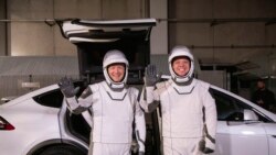 In this Friday, Jan. 17, 2020 photo made available by NASA, astronauts Doug Hurley, left, and Robert Behnken pose in front of a Tesla Model X car during a SpaceX launch dress rehearsal at Kennedy Space Center in Cape Canaveral, Fla. (Kim Shiflett/NASA)