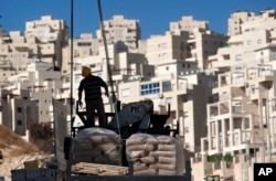 FILE - A worker stands by construction materials to unload at a new housing unit in the east Jerusalem neighborhood of Har Homa, Nov. 2, 2011.