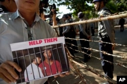A protester displays a picture featuring Myanmar migrants Win Zaw Htun, right, and Zaw Lin near the Thai Embassy in Yangon, Myanmar, Friday, Dec. 25, 2015.