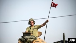 FILE - A soldier gestures as Turkish Army tanks drive to the Syrian-Turkish border town of Jarablus, Aug. 25, 2016