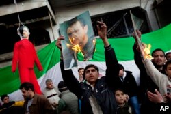 FILE - People burn portraits of Syrian President Bashar Al-Assad during a demonstration on the outskirts of Idlib, northern Syria, Feb. 26, 2012.