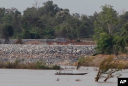 FILE - A fishing boat on the Mekong River passes near a construction site of the Don Sahong dam, near Cambodia-Laos borders, in Preah Romkel village, Stung Treng province, northeast of Phnom Penh, Cambodia, June 20, 2016.