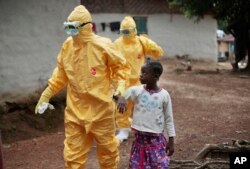 FILE - Health workers accompany a nine-year-old who contracted the Ebola virus to a Monrovia treatment center on Sept. 30, 2014.