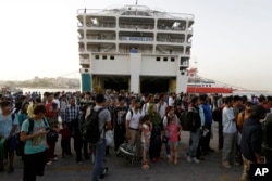 Refugees and migrants wait for a bus, transporting them to the metro station, after their arrival from the northeastern Greek island of Lesbos to the Athens' port of Piraeus, Sept. 7, 2015.