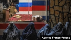 FILE - Afghan burqa-clad women sit in front of a bakery as they seek alms in Kabul, Jan. 6, 2022.