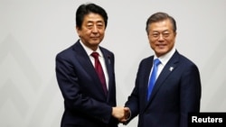 FILE - South Korean President Moon Jae-in shakes hands with Japanese Prime Minister Shinzo Abe during their meeting in Pyeongchang, South Korea, Feb. 9, 2018.