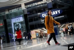 FILE - People walk near foreign brands fashion outlets at a shopping mall in Beijing, China, March 2, 2017.