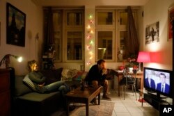 A couple watches a live broadcast television debate with French centrist presidential candidate Emmanuel Macron, right, and far-right candidate Marine Le Pen, in Lyon, central France, May 3, 2017.