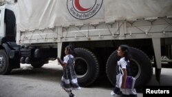 FILE - Girls walk near a Red Crescent aid convoy carrying urgent medical supplies in the rebel-held besieged town of Douma, near in Damascus, Syria, May 26, 2016.