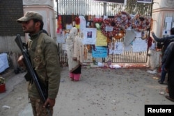 FILE - A soldier stands near a woman reading messages left by people for the victims of the Taliban attack on a school, in Peshawar, Pakistan, Dec. 23, 2014.