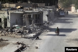 A rebel fighter rides past damaged buildings in al-Rai town, northern Aleppo countryside, Syria, Oct. 2, 2016.