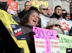 Internal Revenue Service employee Mary Maldonado, of Dracut, Mass. (C) displays a placard during a rally by federal employees and supporters, Jan. 17, 2019, in front of the Statehouse, in Boston, held to call for an end of the partial government shutdown.