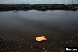 An empty bag of shrimp feed floats on the surface of a stream outside the Sunlight Seafood shrimp farm in Pitas, Sabah, Malaysia, July 6, 2018.