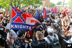 FILE- Members of the white supremacist KKK are escorted by police past a large group of protesters during a KKK rally in Charlottesville, Virginia, July 8, 2017.