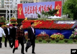 Pedestrians walk by a flower arrangement and billboard with the words "The 7th Congress of the Workers' Party of Korea" in Pyongyang, North Korea, May 5, 2016.
