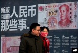 A couple walk past a display showing the security features of the new 100 Yuan note in Beijing, Monday, Jan. 11, 2016.