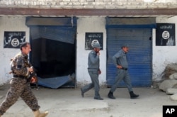 FILE - Afghan police walk past Islamic State militant flags on a wall, after an operation in the Kot district of Jalalabad province east of Kabul, Afghanistan, Aug. 1, 2016. Diminishing in numbers, the group has turned to more sophisticated terrorist attacks in cities.