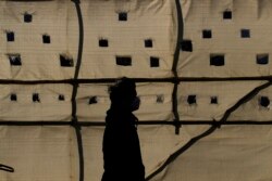 Seorang pria mengenakan masker terlihat seperti siluet saat berjalan melewati lokasi konstruksi di Seoul, Korea Selatan, Rabu, 16 Desember 2020. (Foto AP / Lee Jin-man)