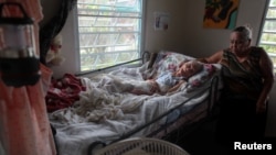 Carmen Rodrigues stands by her bedridden mother, Rosa Maria Torres, 95, after Hurricane Maria destroyed the town's bridge in San Lorenzo, Morovis, Puerto Rico, Oct. 5, 2017. The family are trying to get Torres airlifted out of the town. "If they don't move her, she will die."
