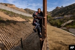 A Honduran migrant grabs his son as they climb the U.S. border fence before jumping into the U.S. to San Diego, Calif., from Tijuana, Mexico, Dec. 22, 2018.