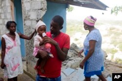 Marc-Sena Docteur feeds his 9-month-old daughter, Size, outside their home damaged in the quake that hit over the weekend in Port-de-Paix, Haiti, Oct. 8, 2018. Docteur’s girlfriend died in the earthquake.