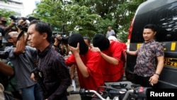 FILE - A plainclothes policeman holds a rifle as he escorts suspects during a police investigation into a men's club after a weekend raid on what authorities described as a "gay spa" in Jakarta, Indonesia, Oct. 9, 2017.
