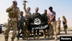FILE - Iraqi security forces and Shi'ite militias pull down a flag belonging to Islamic State militants in Amerli, Sept. 1, 2014.
