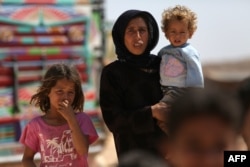 FILE - A woman who fled her village in Syria's Idlib province carries a child at a camp in Kafr Lusin near Syria's border with Turkey, Sept. 9, 2018.