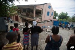 Residents stand looking at a collapsed school damaged by a magnitude 5.9 earthquake the night before, in Gros Morne, Haiti, Oct. 7, 2018.