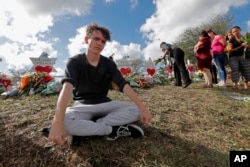 FILE - Chris Grady, a student at Marjory Stoneman Douglas High School, sits at a memorial outside the school in Parkland, Florida, Feb. 19, 2018.