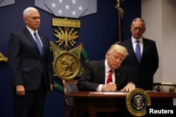 FILE - President Donald Trump signs the initial executive order for a U.S. travel ban, Jan. 27, 2017, at the Pentagon, outside Washington, as Vice President Mike Pence (L) and Defense Secretary Jim Mattis look on.