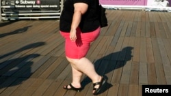 FILE - A woman walks along a boardwalk in New York. The WHO recommends people keep their sugar intake at below 10 percent of their total energy needs.