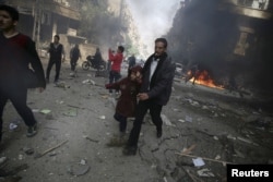 FILE - A man holds the hand of a girl as they rush away from a site hit by what activists said were airstrikes by forces loyal to Syria's President Bashar al-Assad, in the Douma, Syria, Nov. 7, 2015.