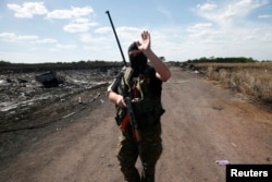 An armed pro-Russian separatist gestures to reporters at the crash site of Malaysia Airlines Flight MH17, near the village of Grabovo, Donetsk region, Crimea, July 21, 2014.