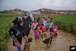 FILE - Rohingya Muslims, who crossed over from Myanmar into Bangladesh, wade past a waterlogged path leading to the Jamtoli refugee camp in Ukhiya, Bangladesh, Nov. 17, 2017.