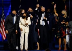 Calon presiden AS dari Partai Demokrat 2020 Joe Biden mengangkat tangan putranya Hunter, saat mereka dan calon wakil presiden Kamala Harris dan keluarga mereka merayakan di atas panggung saat kampanye. (Foto: Reuters / Jim Bourg)