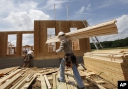 FILE - A construction worker carries a load of wood to a new home as they frame the house in Chester, Virginia, May 16, 2012.