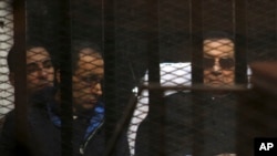 Ousted Egyptian President Hosni Mubarak, 86, lies on a journey, next to his son Gamal, second left, in the defendants cage, during a court hearing in Cairo, Egypt, Saturday, Nov. 29, 2014.