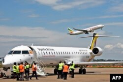 L’équipage au sol prépare un avion Bombadier d’Ouganda Airlines pour le départ, un avion exploité par Ethiopian Airlines décollant en arrière-plan à l’aéroport d’Entebbe lors du lancement du vol inaugural de Uganda Airline vers l’aéroport international Jo