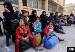 FILE - A picture taken on March 13, 2018 shows evacuated civilians and children sitting in the yard of a school lying on the government side of the Wafideen checkpoint on the outskirts of the Syrian capital Damascus neighboring the Eastern Ghouta enclave.