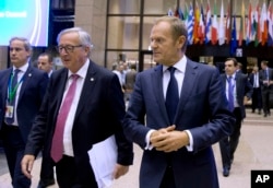 FILE - European Commission President Jean-Claude Juncker, center left, and European Council President Donald Tusk, center right, walk through the atrium during an EU summit in Brussels Oct. 19, 2017.