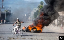 A man rides a bicycle past tires set afire by protesters demanding to know how Petrocaribe funds have been used by the current and past administrations, in Port-au-Prince, Haiti, Oct. 17, 2018.