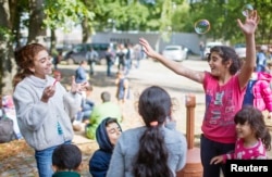 Children of migrants play with soap bubbles after arriving at a new emergency shelter in a sports hall near the Olympiastadion in Berlin, Germany, Sept. 10, 2015.