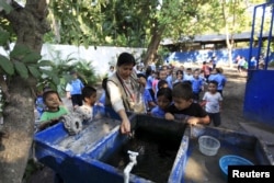 FILE - Health promoter Marielos Sosa deposits fish in a water tank at a local school for a mosquito control project at San Diego village in La Libertad, El Salvador, Feb. 1, 2016.
