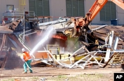 FILE - A worker sprays water to keep down the dust as a giant claw on an excavator rips apart Building 771 at the former Rocky Flats nuclear weapons plant near Golden, Colorado, July 15, 2004.