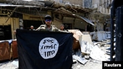 FILE - A member of the Emergency Response Division holds an Islamic State militants flag in the Old City of Mosul, Iraq, July 10, 2017.