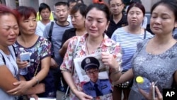 FILE - In this image taken from a video footage from AP Video, a woman holds up a photo of her son, a missing firefighter, outside a hotel where officials held a daily media conferences in northeastern China's Tianjin municipality, Aug. 16, 2015.