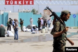 FILE - A Kurdish People's Protection Units (YPG) fighter walks near residents who had fled Tel Abyad, as they re-enter Syria from Turkey after the YPG took control of the area, at Tel Abyad town, Raqqa governorate, Syria, June 23, 2015.